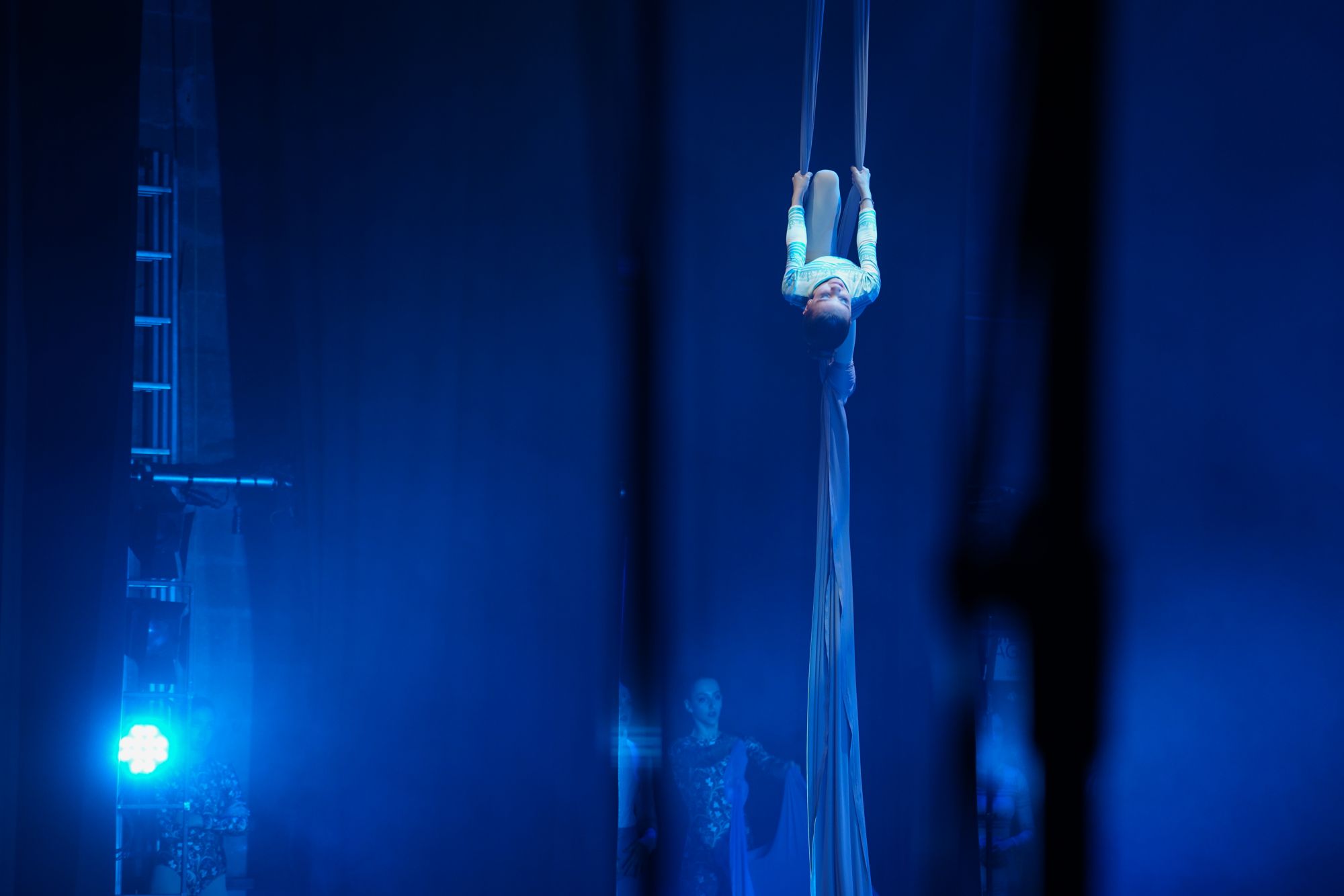 Acrobata sui tessuti aerei in una luce blu teatrale