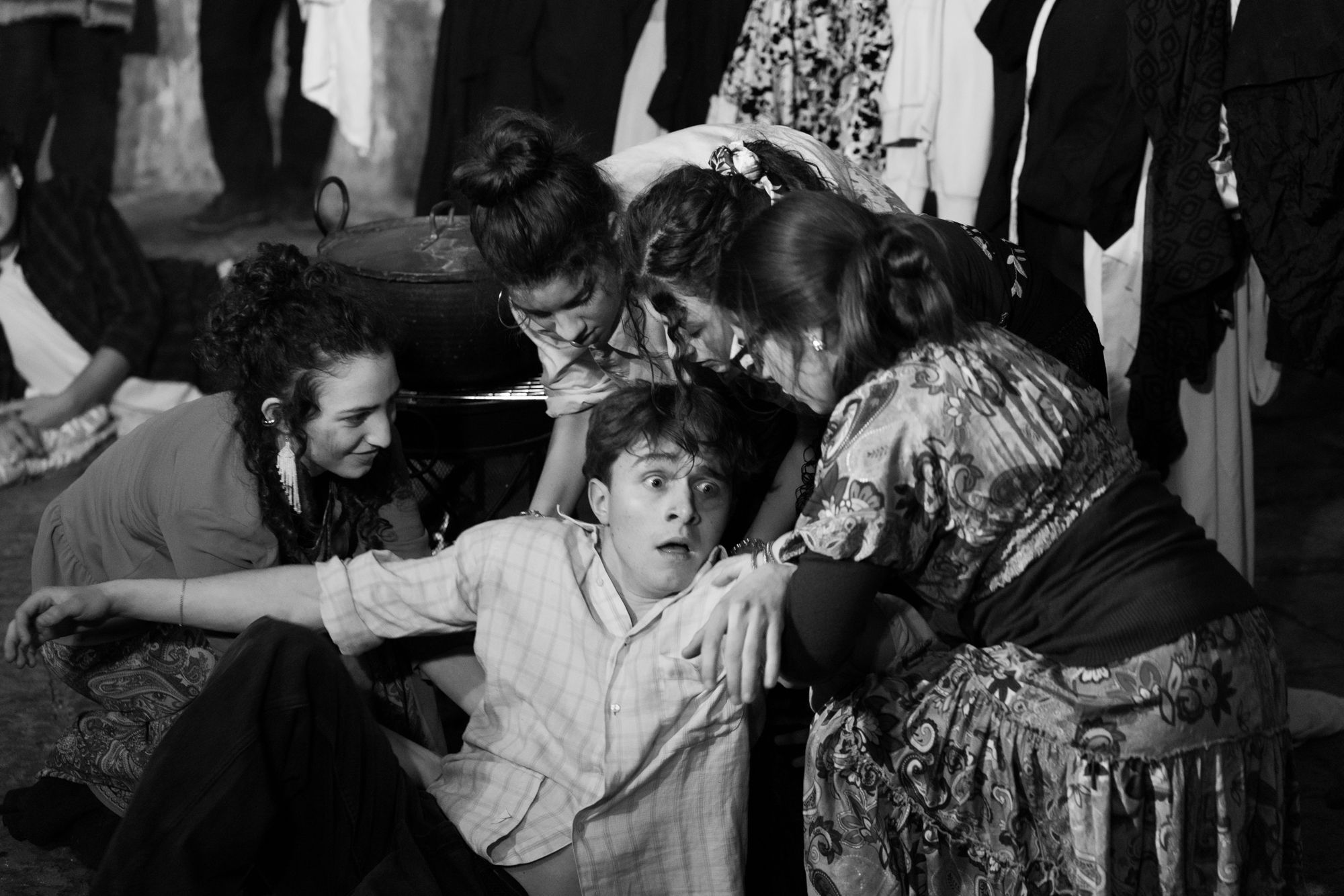 Scena corale di uno spettacolo teatrale in bianco e nero: attrici attorno al protagonista